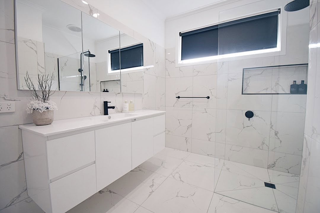 Modern bathroom with white marble tiles, floating vanity, and glass shower enclosure with black fixtures and accents