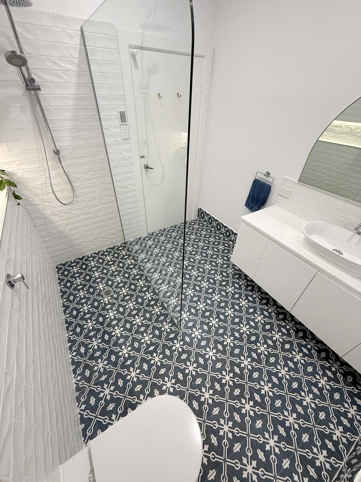 Modern bathroom with walk-in shower, white subway tile walls, black and white patterned floor tiles, and floating vanity with mirror.