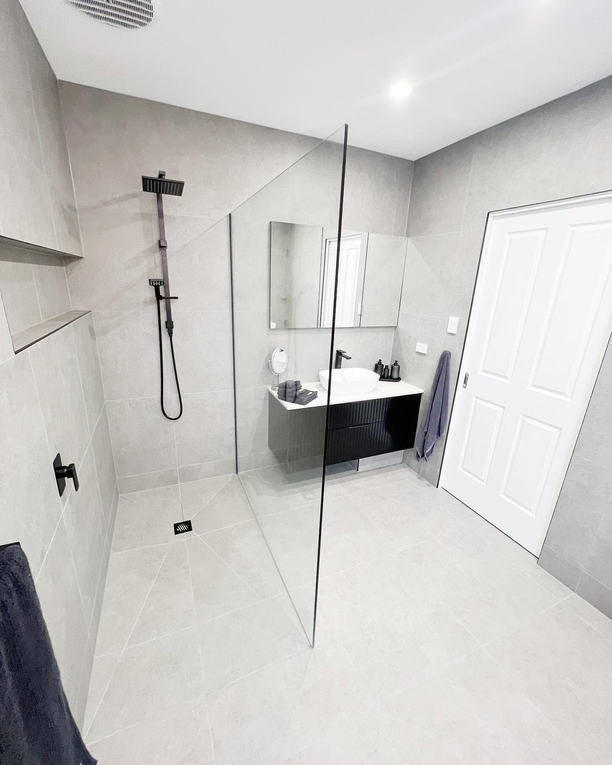 Modern bathroom with walk-in shower, black vanity with white sink, white subway tile walls, and minimalist design.