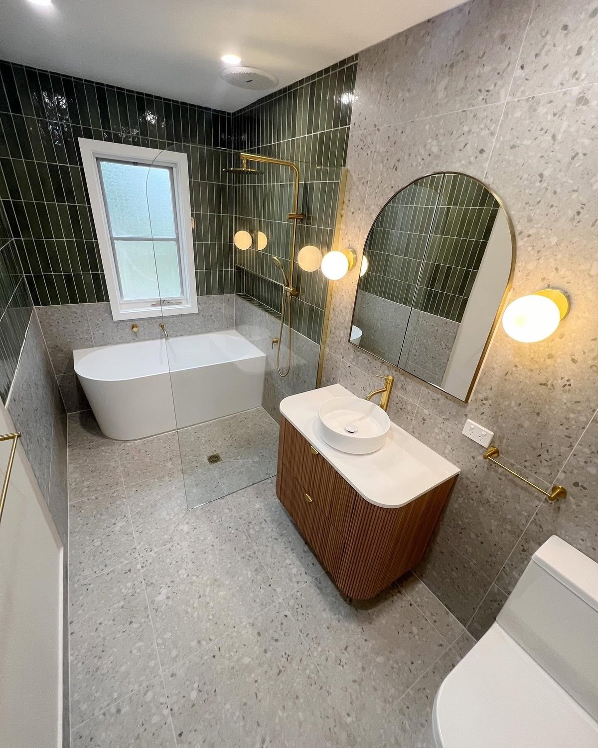Bathroom makeover with white soaking tub, wooden vanity with mirror, terrazzo flooring and black tile shower area
