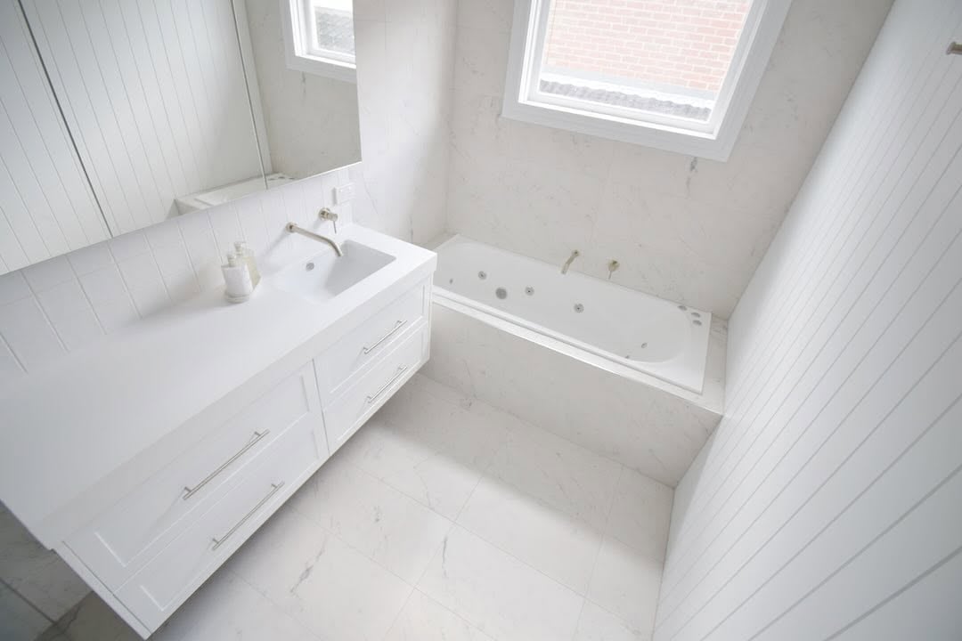 Modern white bathroom with vanity sink, mirror, bathtub with jets, and skylight windows