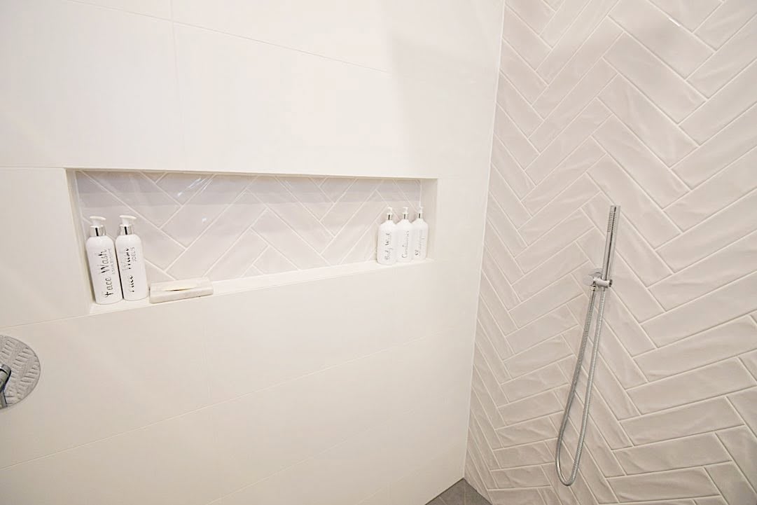 Modern bathroom shower niche with white herringbone tile wall and chrome shower head