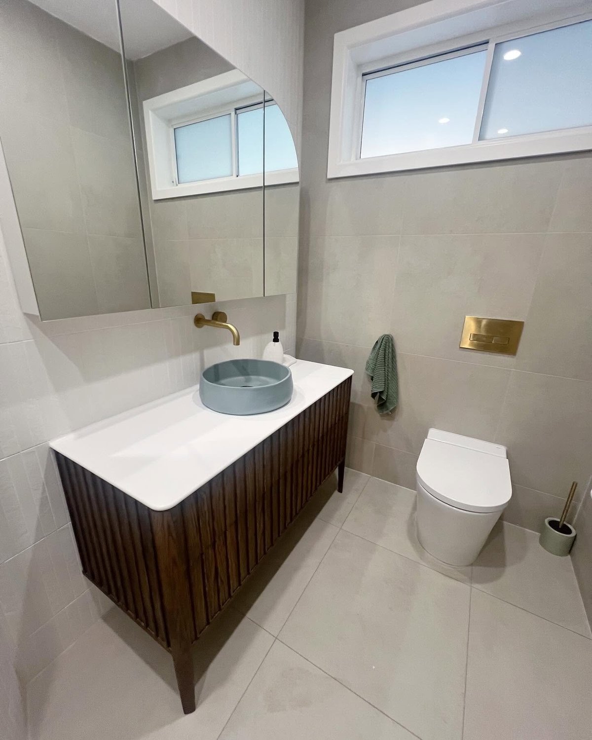Modern bathroom with wooden vanity, round vessel sink, large mirror, toilet, and windows providing natural light