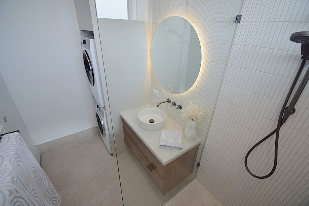Modern bathroom with illuminated oval mirror, floating vanity with white sink, and shower head visible on right side