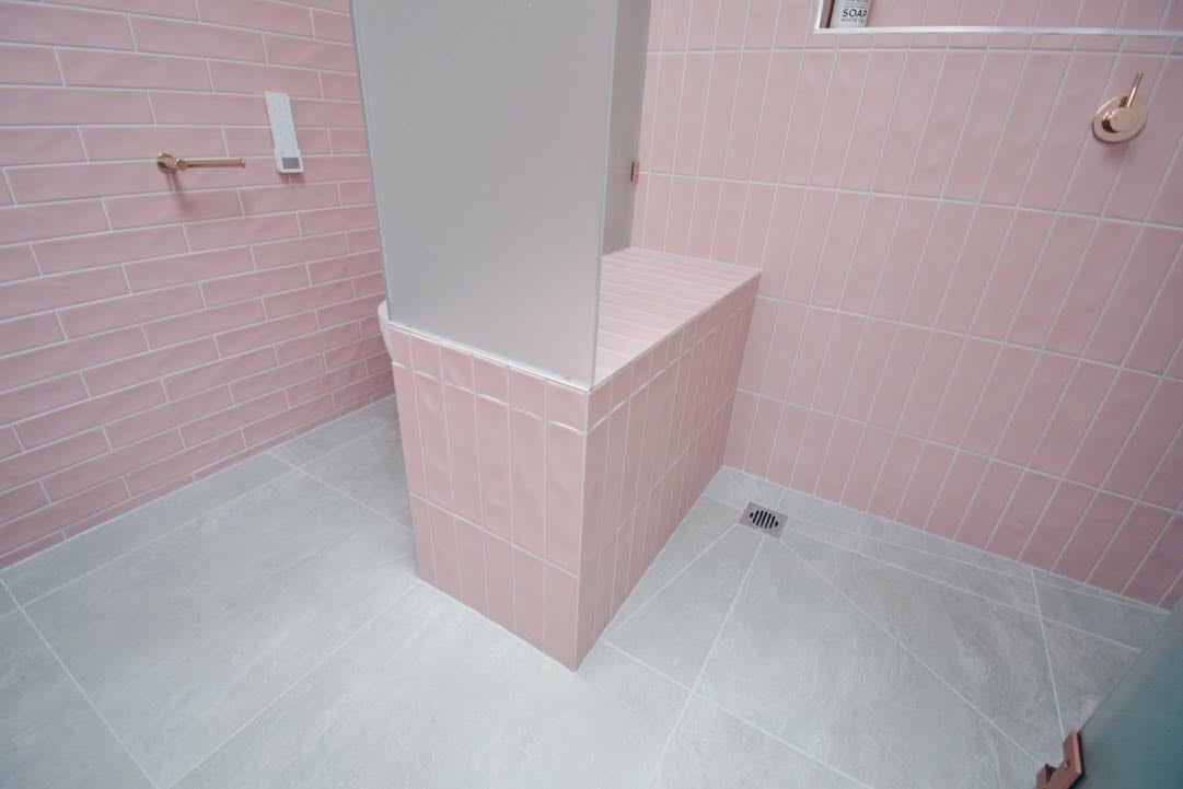 Modern bathroom with pink subway tile walls, white column structure, light gray tile flooring, and drain fixture